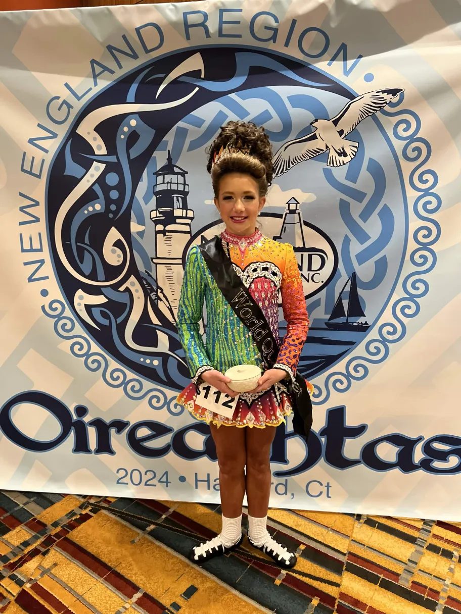 Spirited Soles dancer holding an award in front of the New England Region Oireachtas banner