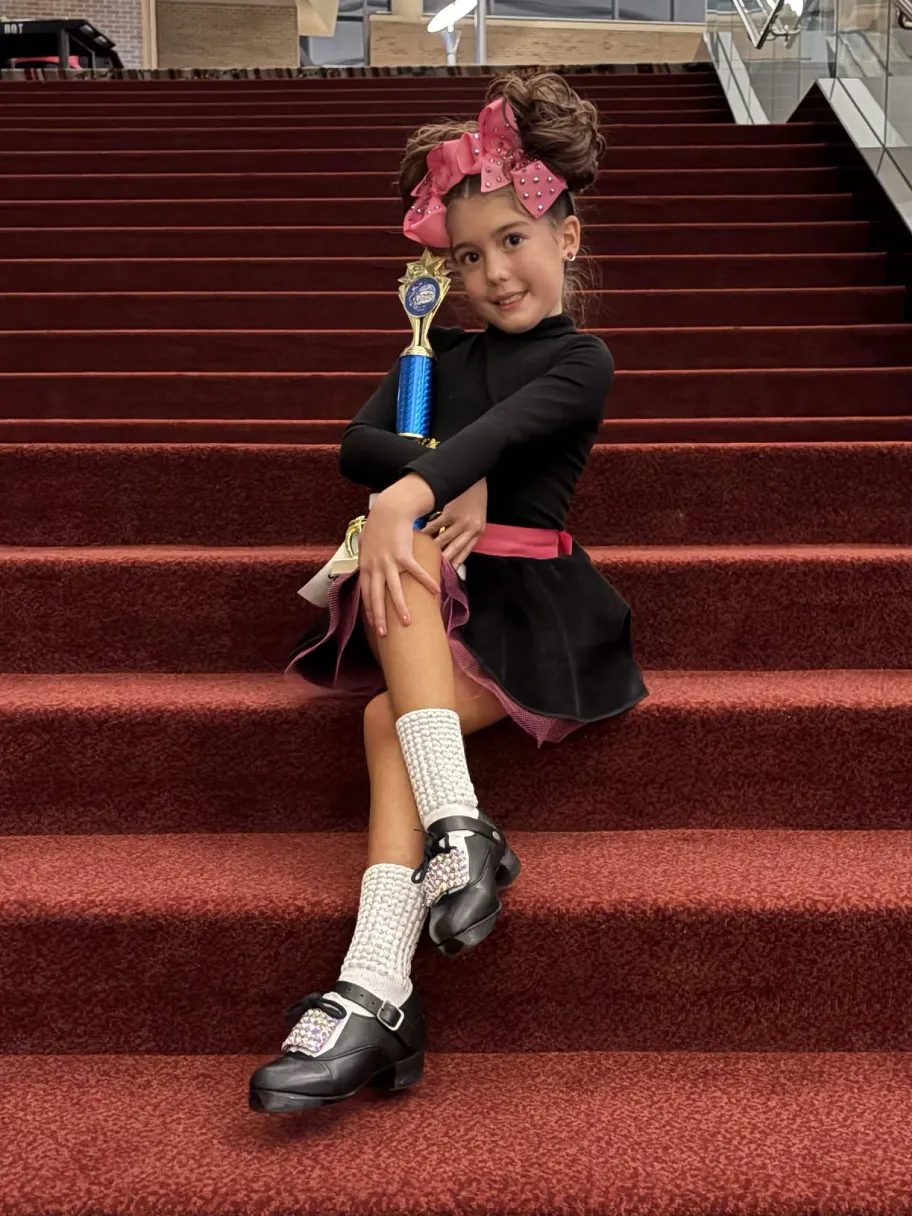 Young dancer sitting on red stairs holding a trophy
